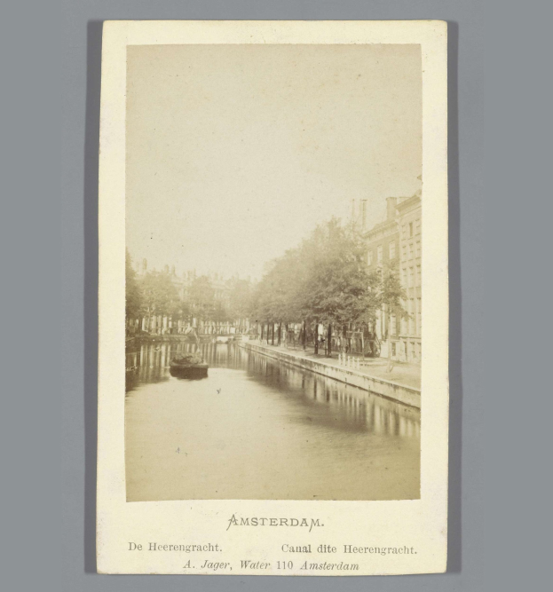 Altes Schwarz-Weiß-Foto eines Kanals in Amsterdam mit einem Boot auf dem Wasser, Bäumen an den Ufern und Gebäuden im Hintergrund; Text erscheint unten.
