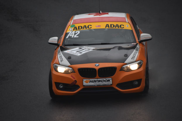 Ein oranges BMW-Auto mit sportlichem Text und Zahlen, das auf einer Rennstrecke fährt.