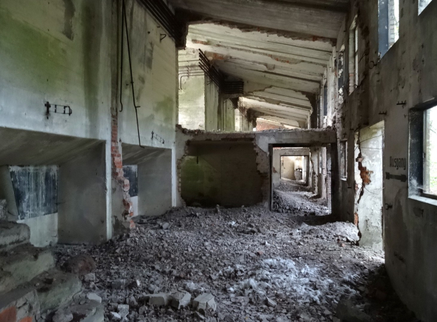 Altes Gebäude mit ausgedehnten Trümmern, zerbrochene Fenster und verstreute Trümmern, was auf große Verwahrlosung hindeutet.