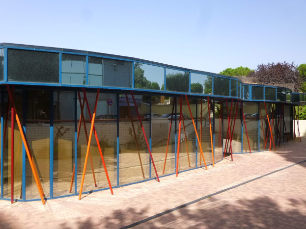 Ein modernes Schulgebäude mit zahlreichen Fenstern, einem vorderen Baumgang und einem klaren blauen Himmel.