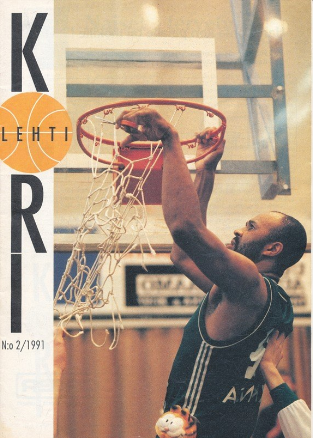 Ein Basketballspieler taucht den Ball in den Korb mit einem Netz im Hintergrund, während eine andere Person daneben an einer Wand steht, mit einer Kobe Bryant Basketballkarte links sichtbar.