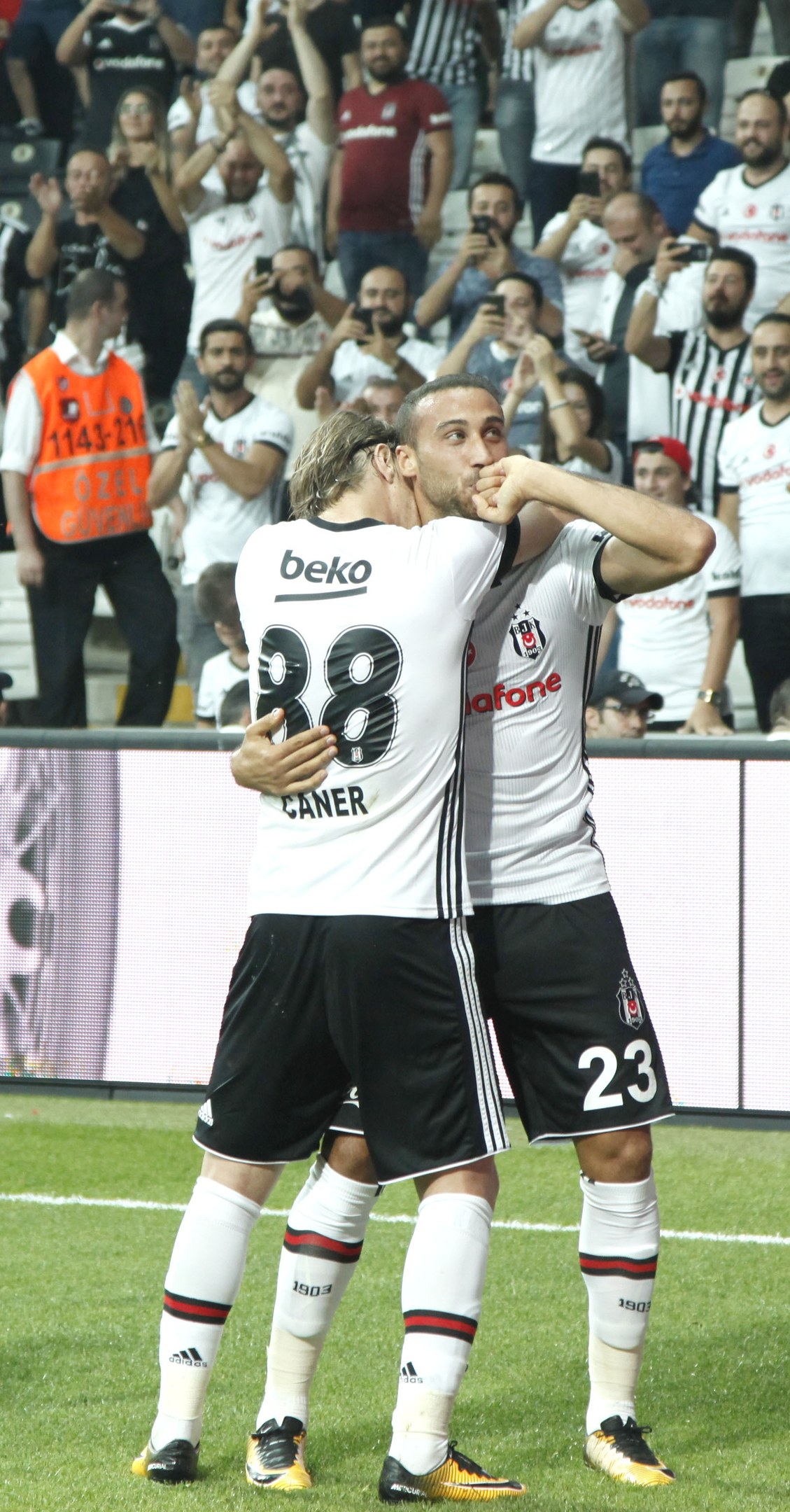 Two soccer players embracing after scoring a goal, with a cheering crowd in the background.