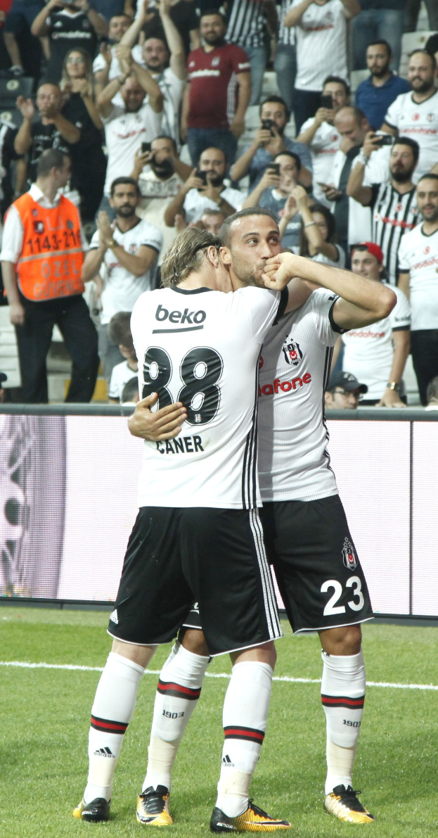 Two soccer players embracing after scoring a goal, with a cheering crowd in the background.