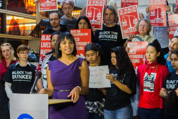 Frau an einem Rednerpult mit Mikrofon, spricht zu einer Menge mit Schildern, als Black Lives Matter-Aktivistin identifiziert.