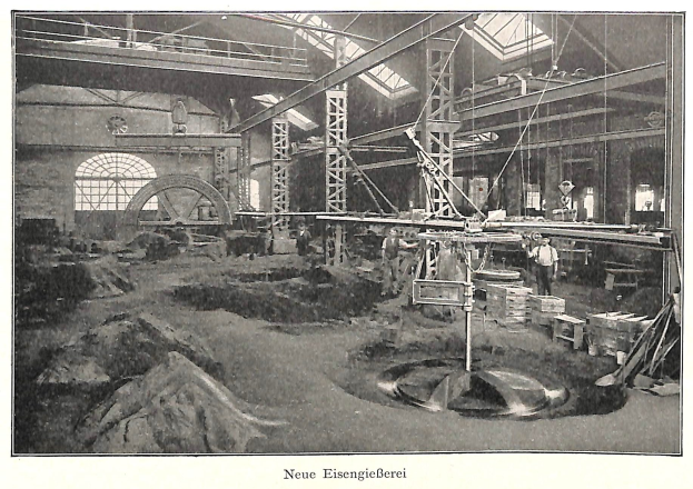 Schwarzes und weißes Foto einer Fabrikinnenansicht mit Arbeitern, die Maschinen bedienen, Metallstangen und -stangen, beschriftet mit "Neue Eisenglebeerei, die erste Fabrik in Deutschland" unten.