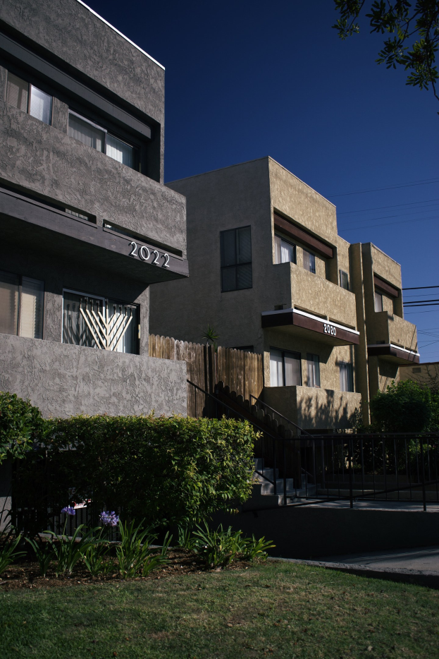 Eine Reihe von Wohngebäuden in San Francisco, Kalifornien, mit sichtbaren Fenstern, Grünflächen, einem Zaun, Treppen, einem Baum, Überlandleitungen und einem Himmel als Hintergrund.