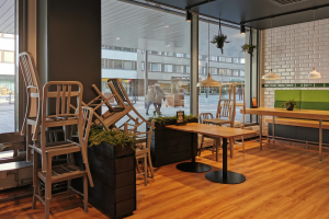 Ein Restaurantinnenraum mit Holztischen und -stühlen, sichtbar durch ein großes Fenster, das eine Straßenszene in Berlin, Deutschland, zeigt.