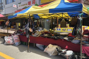 Ein Straßenmarkt mit Zelten, die Taschen, Hüte und andere Artikel präsentieren, vor Gebäuden mit Fenstern und Texttafeln im Hintergrund.