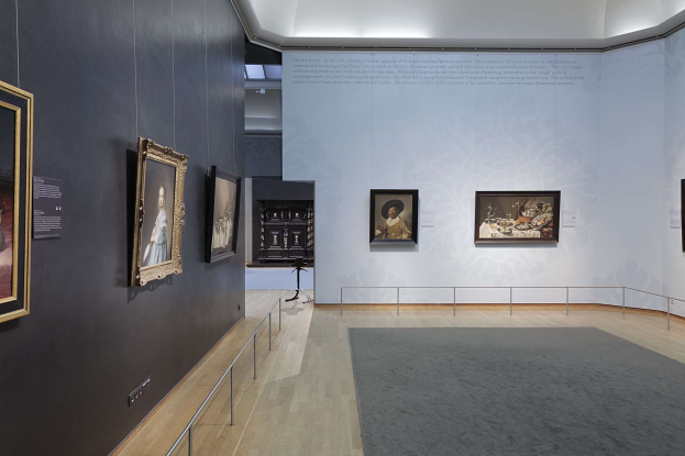 Ein prächtiger Raum in der Nationalgalerie in London, gefüllt mit zahlreichen Gemälden an den Wänden, einem Teppichboden, Geländern und einer Decke mit Beleuchtung.