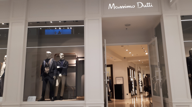 Vitrine des Massimo Dutti in Mailand, Italien, mit Schaufensterpuppen in moderner Kleidung, beleuchteter Decke, Texttafeln und sichtbarem Boden.