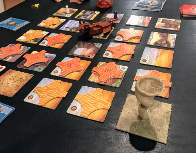 Ein unordentlicher Tisch mit Star Wars: The Old Republic-Brettspielkarten, Spielzeugen und Gegenständen in einem Raum mit einer Wand im Hintergrund.