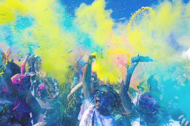 Menschen feiern Holi-Fest mit farbigem Pulver in der Luft vor einem hellblauen Himmel.