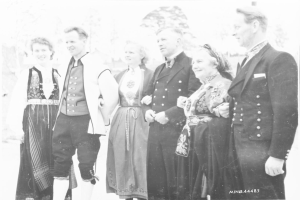 Eine Gruppe von Menschen in den 1930er Jahren, die zusammen draußen stehen, lächeln und Bäume im Hintergrund haben, mit dem Text 'Bayerische Familie in den 1930er Jahren' unten.