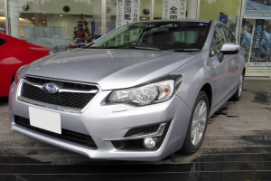 Silberner Wagen vor einem roten Auto mit einer Glaswand im Hintergrund, die einen Weihnachtsbaum, Lichter und Plakate mit Autofotos und Text zeigt.