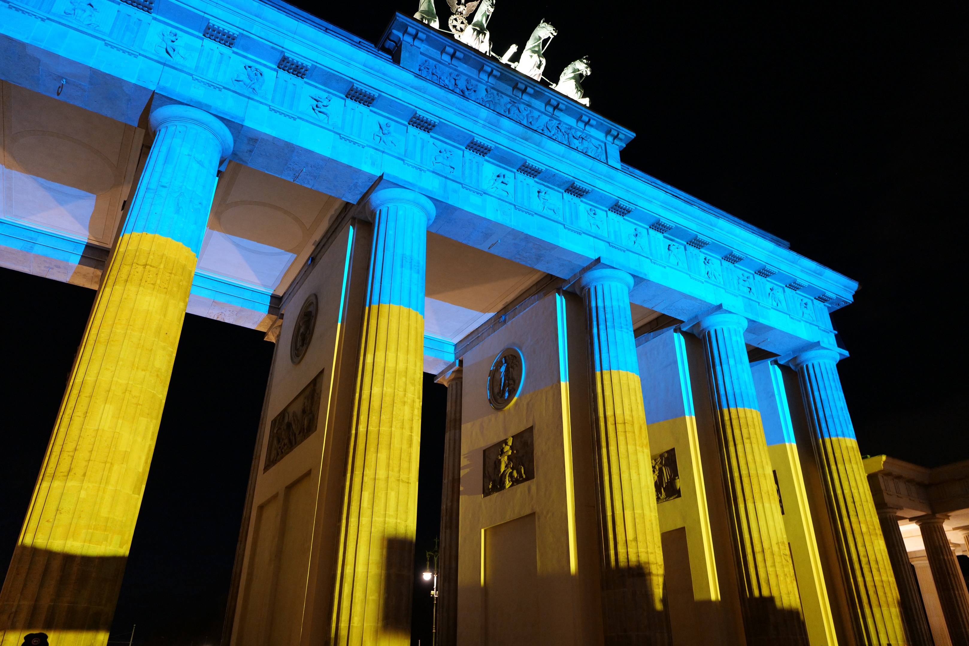 Das Brandenburger Tor in Berlin, Deutschland, erstrahlt in Blau und Gelb und präsentiert sich vor einem dunklen Hintergrund mit seinen Skulpturen.