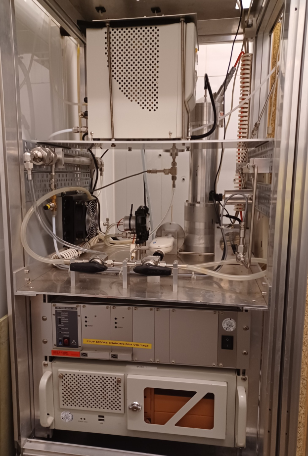 Eine Maschine, wahrscheinlich eine Testkammer, befindet sich in einem Metallschrank in einem Raum, mit verschiedenen Komponenten und Kabeln, die daran angeschlossen sind, und einer Wand im Hintergrund.