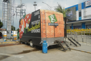 Lastwagen vor einem Geb\303\244ude mit einer Tafel, auf der "Teilen Sie eine positiver Uberladene Erfahrung" steht, mit Stufen, einem Zylinder am Boden, Gel\303\244ndern, Strommasten mit Dr\303\244hten, Laternenmasten, B\303\244umen und einem bew\303\266ltigten Himmel.