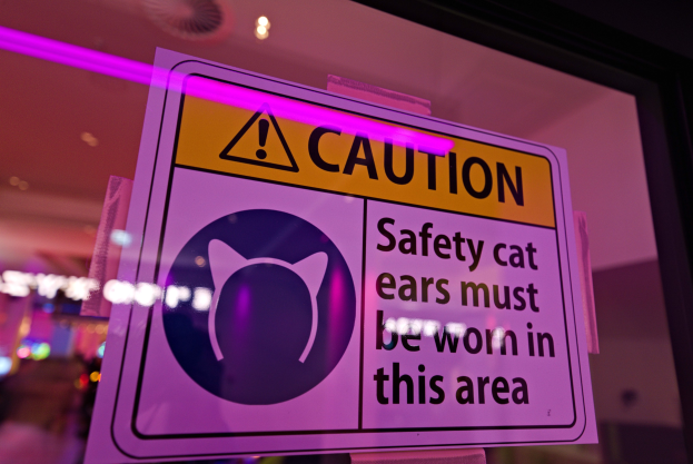 Eine Warnschilder in einem Ladenschaufenster lautet "Vorsicht: Sicherheitskatzenohren müssen in diesem Bereich getragen werden." vor einem unscharfen Hintergrund.