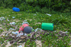 Ein Strand voller Plastikflaschen, Dosen und anderem Müll mit Pflanzen und Bäumen im Hintergrund.