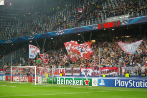 Ein Fuballspiel wird in einem gut beleuchteten Stadion mit einer groen Menge, grnem Rasen, einem mit Bannern geschmckten Tor und einem Bildschirm in der linken oberen Ecke gespielt.